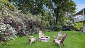 A well-maintained grassy area with a stone fire pit and Adirondack chairs.