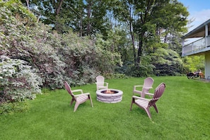 Un área verde cuidada con un hogar de piedra y sillas Adirondack.