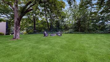 A well-maintained grassy lawn with two Adirondack chairs and a stone fire pit.
