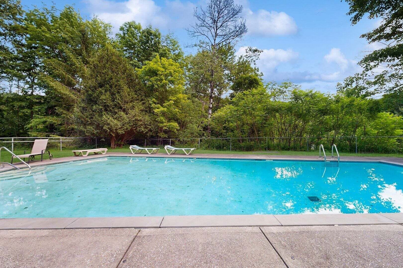 Piscina con sillas de descanso y una valla, rodeada de árboles.