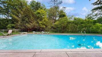 Piscina con sillas de descanso y una valla, rodeada de árboles.