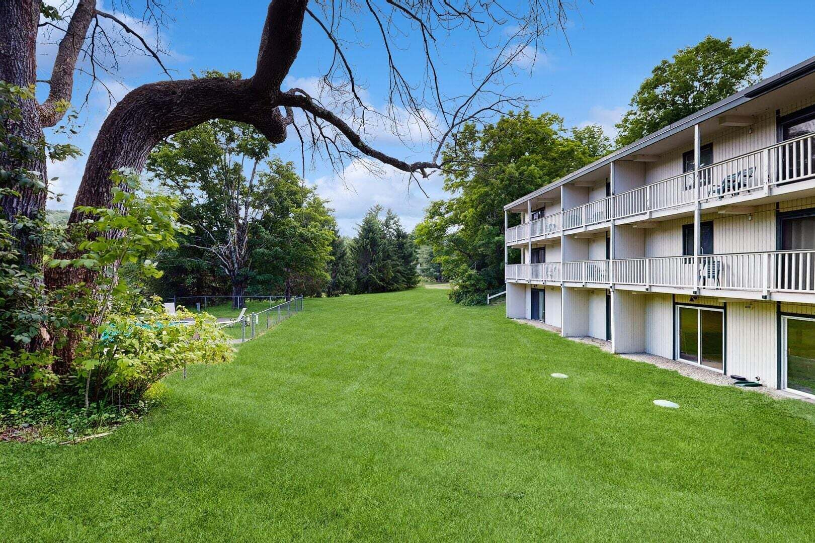 Un edificio de varios pisos con balcones, un césped bien cuidado y árboles al fondo.