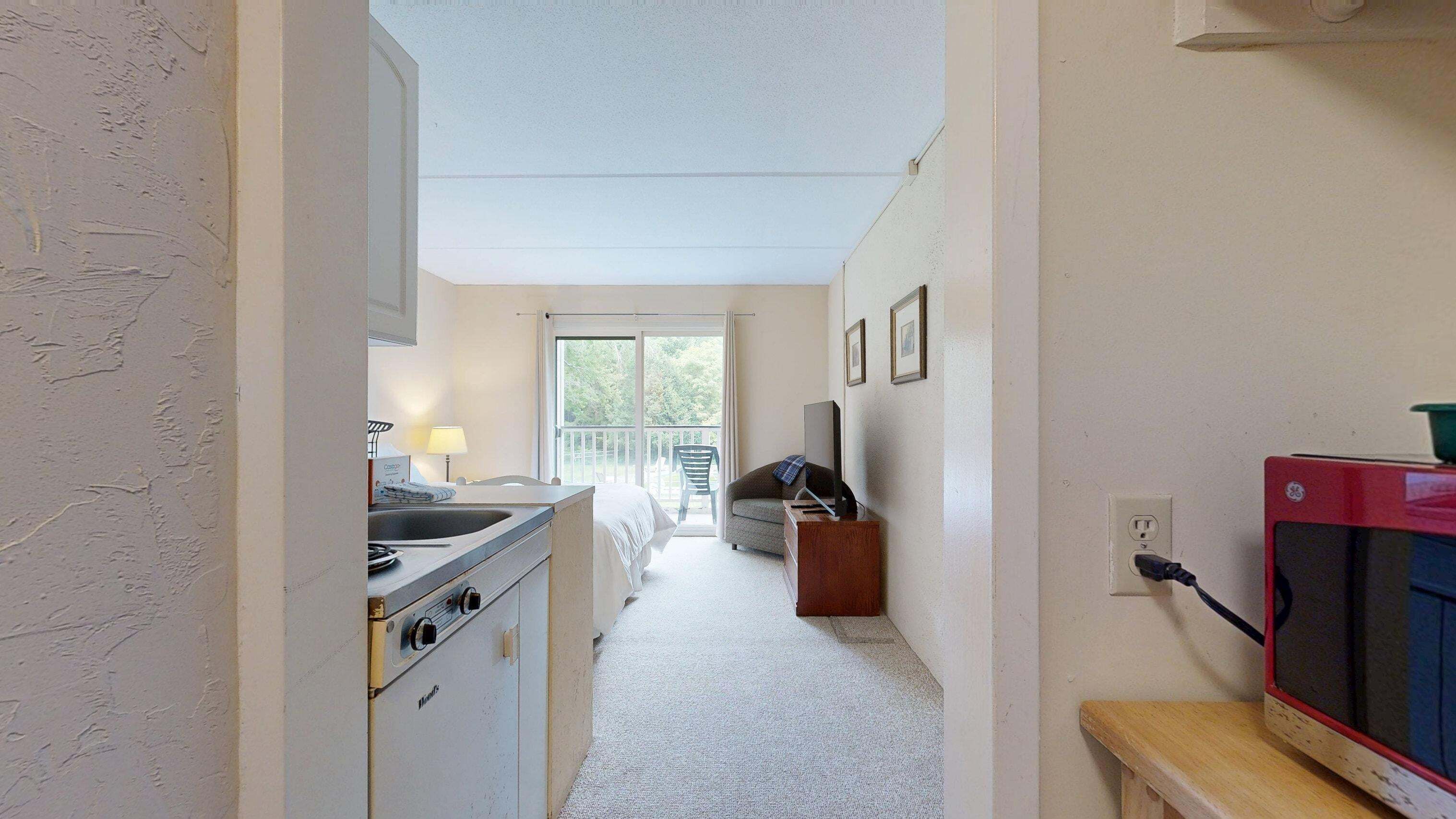 Un couloir étroit mène à un balcon d’où l’on peut admirer les arbres. On y trouve également une petite cuisine équipée d’une cuisinière, une chaise et un téléviseur.