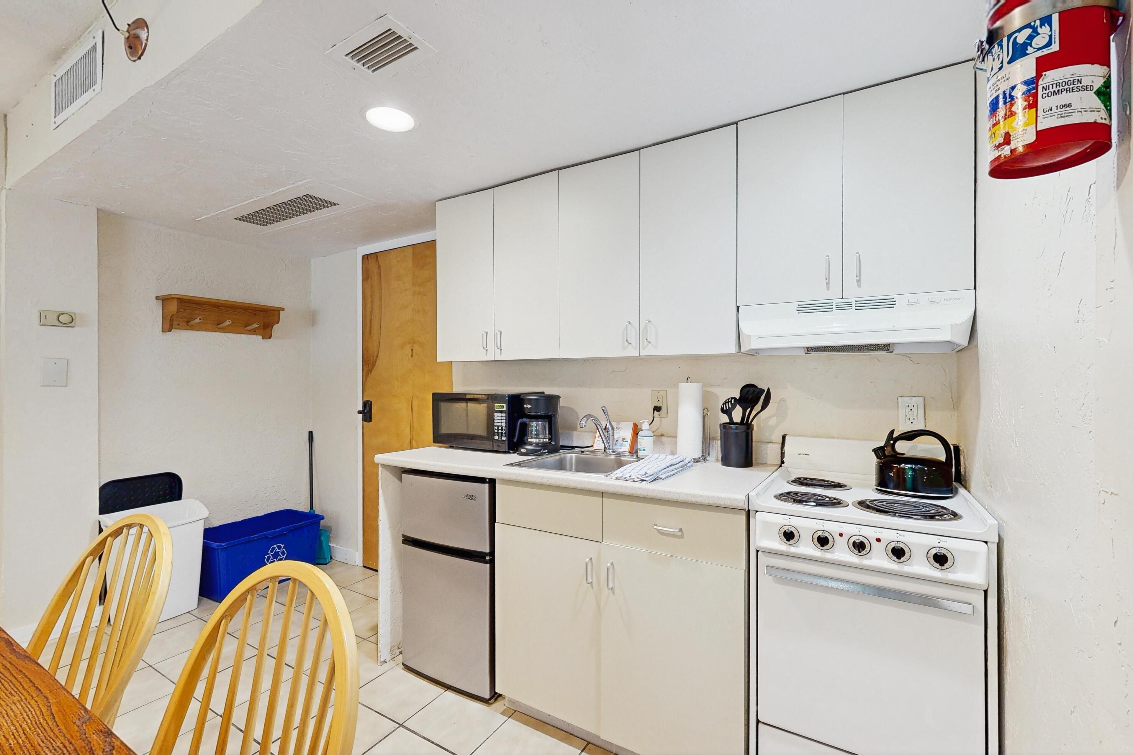 Cocina compacta con gabinetes blancos, estufa, microondas y cafetera.