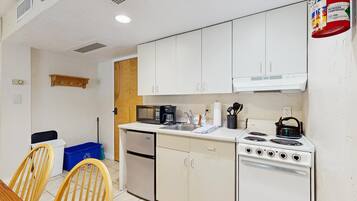 Cocina compacta con gabinetes blancos, estufa, microondas y cafetera.