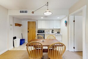 A compact kitchen with white cabinets, a microwave, and a stove. There is a dining table with four chairs. - Sugarbush-area condo with private queen bedroom and seasonal pool (Warren)