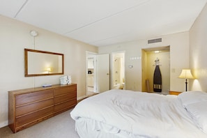 A hotel room with a large bed, a wooden dresser, a mirror, and a bathroom visible through an open door. - Sugarbush-area condo with private queen bedroom and seasonal pool (Warren)