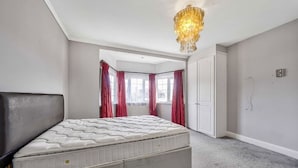 A bedroom with a large bed, a chandelier, a wardrobe, and a window with curtains. - Ldn-hend in London With 3 Bedrooms and 1 Bathrooms (London)