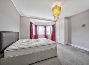 Ein Schlafzimmer mit einem großen Bett, einer Chandelier, einem Kleiderschrank und einem Fenster mit Vorhängen.
