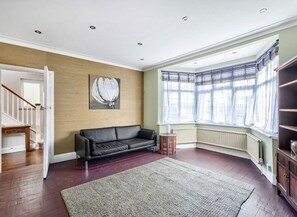 Ein geräumiges Wohnzimmer mit einer schwarzen Ledersofa, Holzboden, einem großen Fenster mit Vorhängen und einem Gemälde an der Wand.