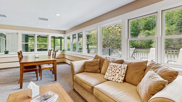 A spacious room with a large window, a dining table, and a sofa. - Four Season Condo:  seasonal pool, ski, hike & golf (Warren)