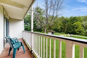 A balcony with two chairs, a small shed, and a pool area with lounge chairs.