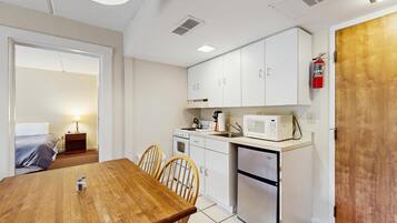 Cocina compacta con armarios blancos, microondas, estufa y refrigerador. Hay una mesa de comedor de madera con sillas.