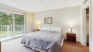 A bedroom with a large bed, two bedside tables with lamps, a window with a view of greenery, and a door leading to a closet. - Four Season Condo:  seasonal pool, ski, hike & golf (Warren)