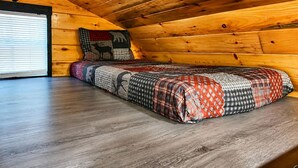 Ein gemütliches Blockhäuschen-Zimmer mit Holzbalkendecke, einem Bett mit gemustertem Quilting und einer Bärenkopfdarstellung an der Wand.