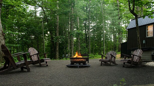 Eine Waldszene mit Lagerfeuer und Adirondack-Stühlen.