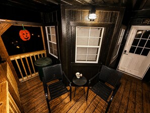 A wooden deck with two black metal chairs and a small table, a white door, and a window with blinds. - Escape to Black Bear Cabin near Red River Gorge, your private woodland retreat. (campton)
