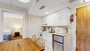 A compact kitchen with white cabinets, a microwave, a stove, and a refrigerator. There is a wooden dining table with chairs. - Four Season Connecting Condos:  seasonal pool, ski, hike & golf (Warren)