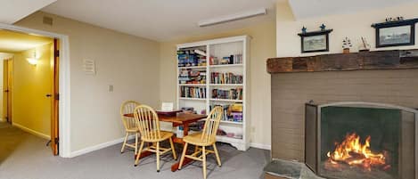 A living room with a fireplace, a bookshelf, and a dining area with chairs.
