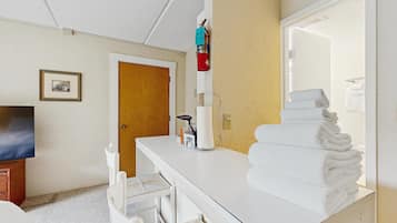Habitación de hotel con tocador blanco, espejo, montón de toallas, televisor y puerta.