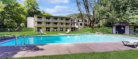 A hotel with a swimming pool, outdoor seating, and a building with multiple balconies.