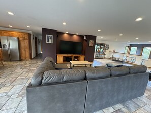 Un salon moderne avec un canapé d’angle, un téléviseur à écran plat, des meubles en bois et un coin repas équipé d’une banquette.