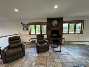 Ein geräumiges Wohnzimmer mit Kamin, zwei Ledersesseln, einem Couchtisch und einer Wanduhr.