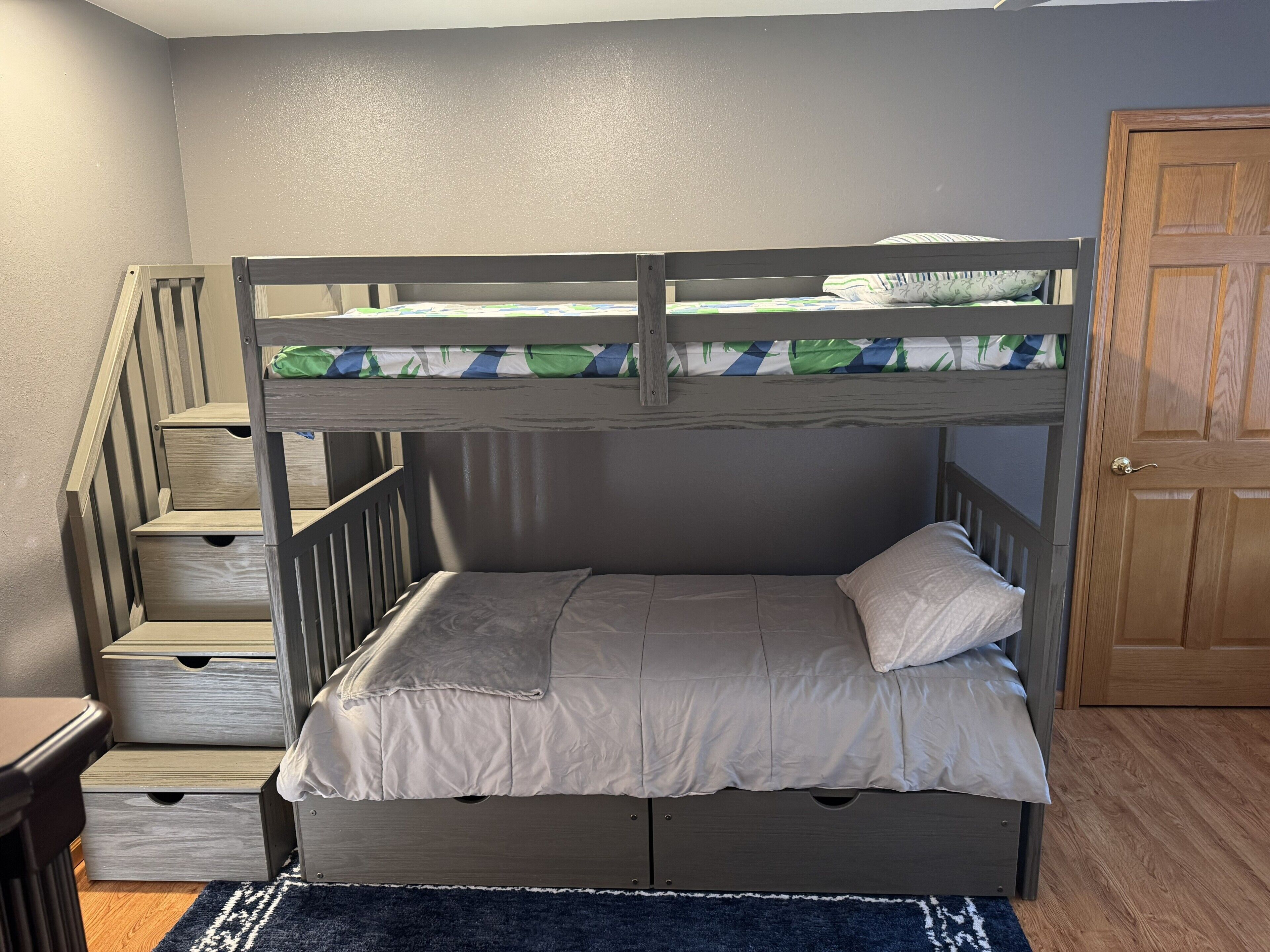 Un lit superposé avec une structure en bois, un lit inférieur avec un oreiller et un escalier avec des tiroirs.
