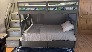 Ein Stockbett mit Holzrahmen, ein Bett unten mit Kissen sowie eine Treppe mit Schubladen.