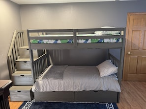 Ein Stockbett mit Holzrahmen, ein Bett unten mit Kissen sowie eine Treppe mit Schubladen.