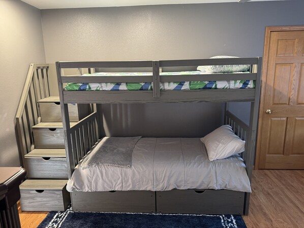 A bunk bed with a wooden frame, a lower bed with a pillow, and a staircase with drawers.