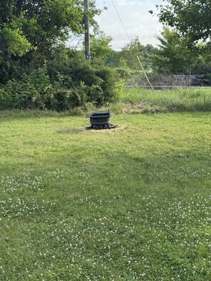A grassy field with a metal fire pit in the center.