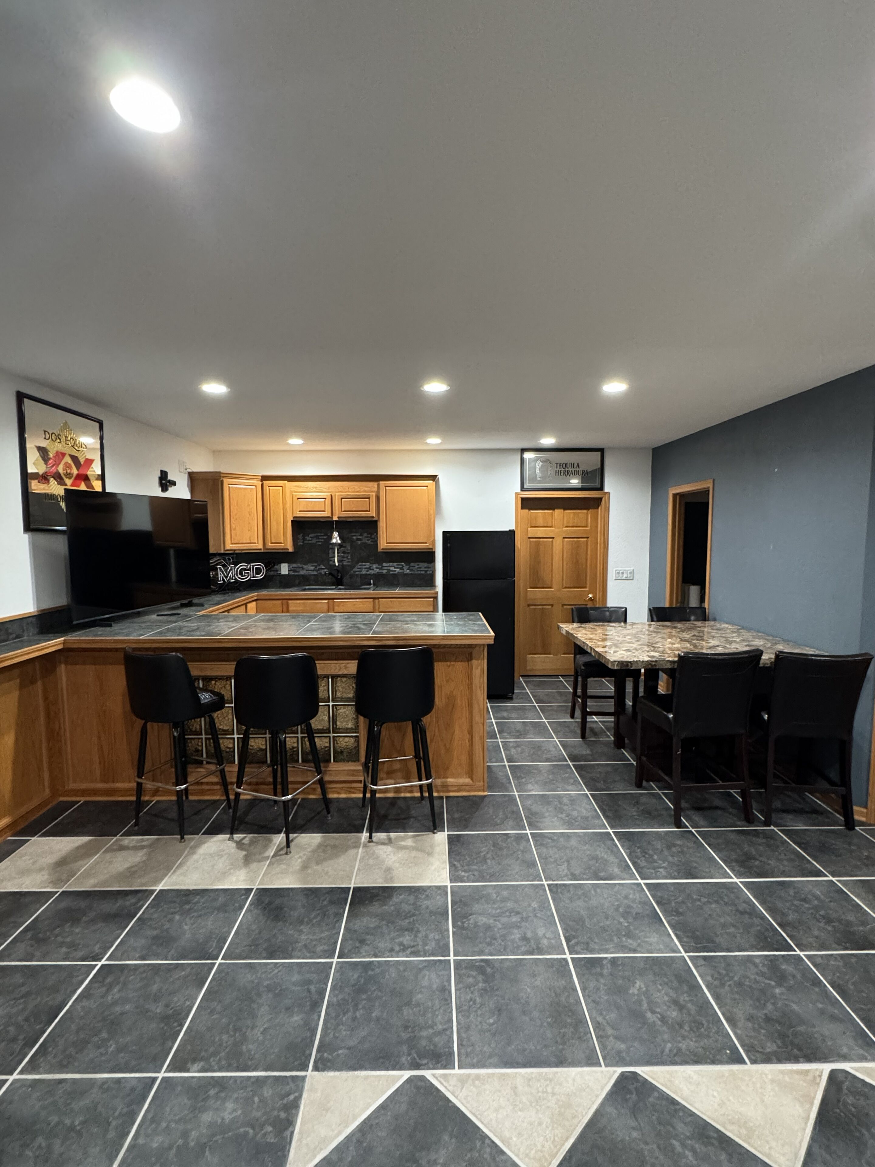 Una cocina moderna con una isla central, taburetes de bar, una mesa de comedor con sillas, armarios de madera y un refrigerador.