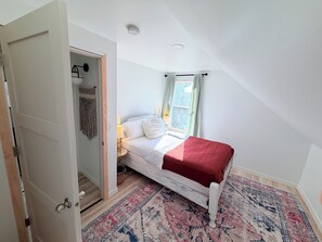 A bedroom with a bed, a window with curtains, a door, and a patterned rug.