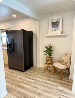 A modern kitchen with a large black refrigerator, a wicker side table with a plant, and a chair with a cushion.
