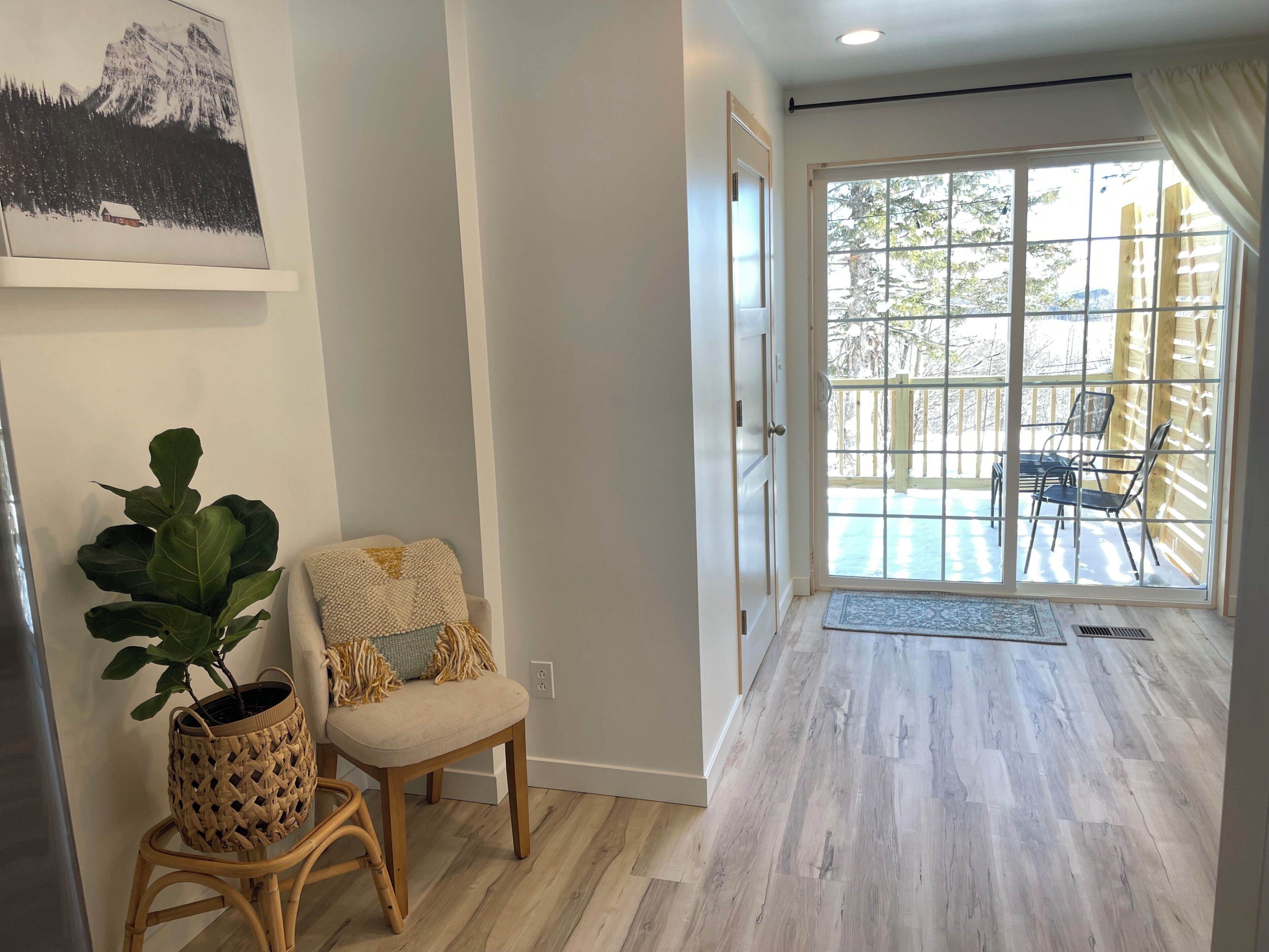 A hallway with a wicker chair, a potted plant, and a framed picture on the wall.
