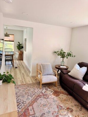 Un salon moderne avec un canapé en cuir marron, une chaise en bois, un tapis à motifs et un coin repas comprenant une table et des chaises.