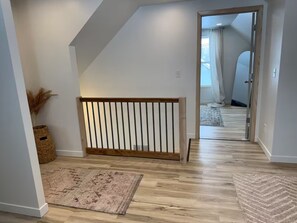 Ein Flur mit Holzbalkon, einem gemusterten Teppich und Blick in einen weiteren Raum mit Tür und Fenster.