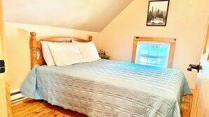 Une chambre à coucher avec un lit en bois, une couvre-lit matelassée et une fenêtre donnant sur des arbres.
