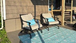 Deux chaises d’extérieur avec coussins, un tapis à motifs et une terrasse en bois dotée d’une rambarde.