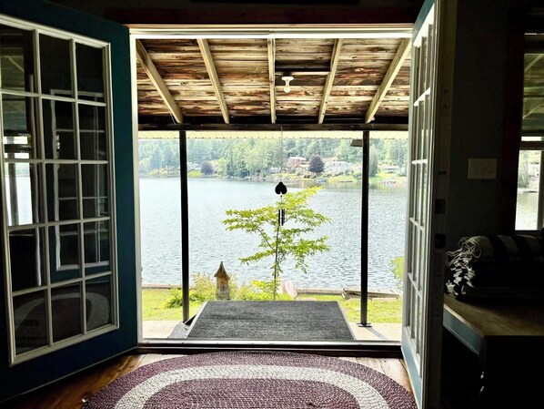 A room with a view of a lake, a wooden ceiling, and a door leading outside.
