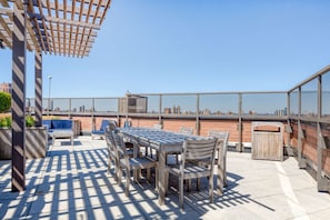 Eine Dachterrasse mit Tisch und Stühlen, einer Pergola und Blick auf die Stadtlandschaft.