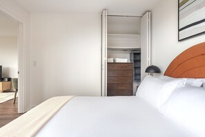 Um quarto com uma cama, guarda-roupa, escrivaninha e televisão.