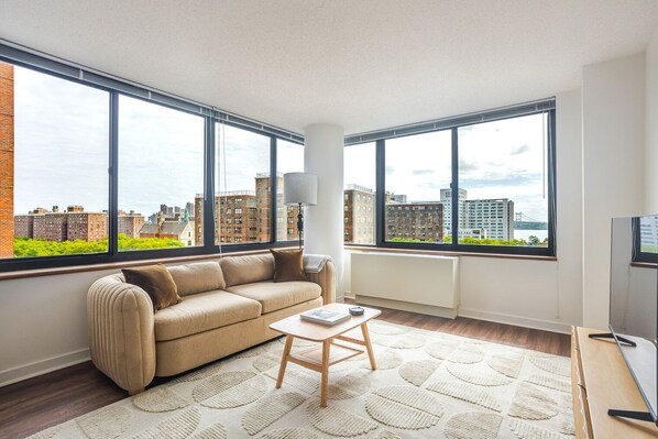 Ein modernes Wohnzimmer mit einer Couch, einem Couchtisch und großen Fenstern mit Blick auf die Stadt.