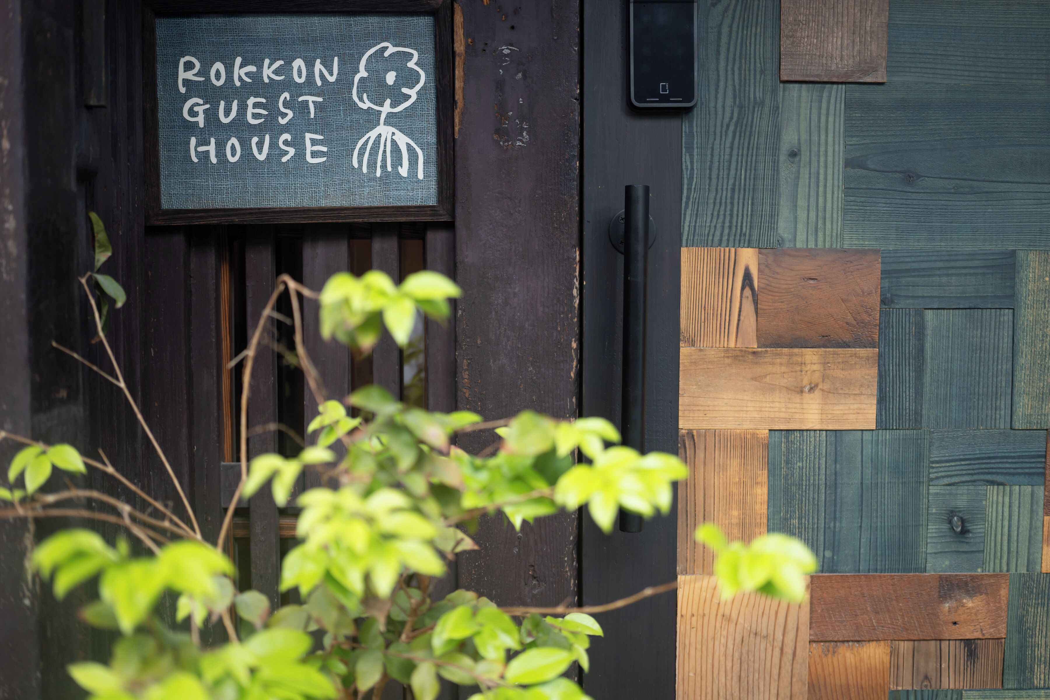 A wooden door with a sign that reads 'ROKKON GUEST HOUSE' and a black intercom system.