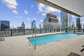 A rooftop pool with a city skyline view, a glass railing, and a sign indicating the pool's depth. - Blueground | Midtown South, gym, nr Times Square (New York)