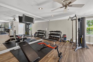 Ein Fitnessraum mit Trainingsgeräten, einem Fernseher und einem Deckenventilator.