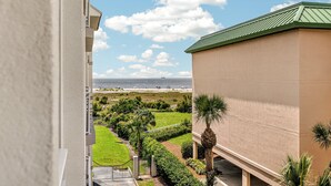 Uitzicht vanaf een balkon op een strand, met een heldere lucht en enkele wolken.