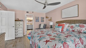 Een slaapkamer met een bed, plafondventilator, dressoir, deur en een wand met kunstwerken.