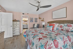 Ein Schlafzimmer mit einem Bett, einem Deckenventilator, einem Schminktisch, einer Tür und einer Wand mit Kunstwerken.